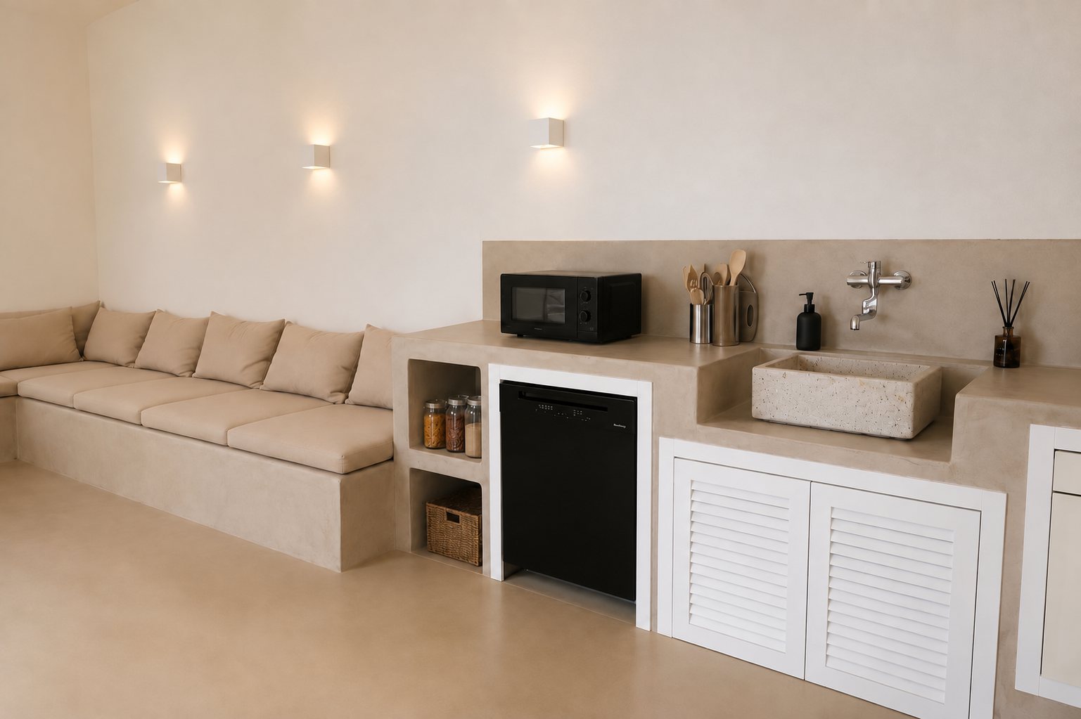 Là où la banquette rejoint la cuisine à Casa Andrea — un seul bloc continu de microciment, trois appliques de plâtre au-dessus de l'assise, un évier de pierre à robinetterie murale, un micro-ondes et des portes persiennées, des bocaux et un panier dans la niche ouverte, Pouilles.