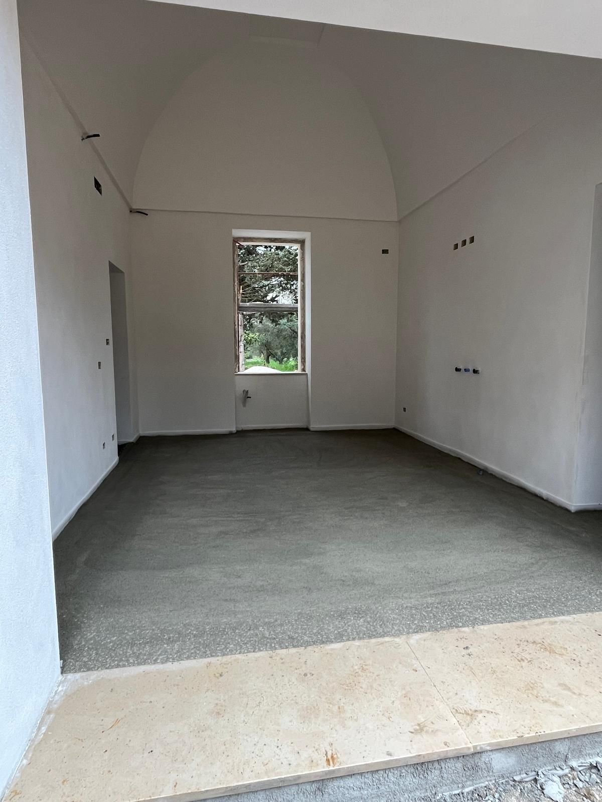 The restored barrel-vaulted master bedroom of Casa Andrea's original casale, fresh white lime plaster, original arched window framing an olive tree.