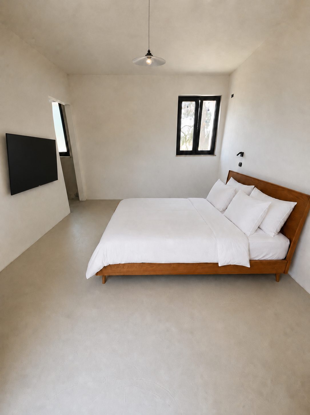 La première chambre en suite de Casa Andrea — murs et sol en microciment d'un ton chaud, lit en bois et linge blanc, fenêtre à cadre noir, Pouilles.