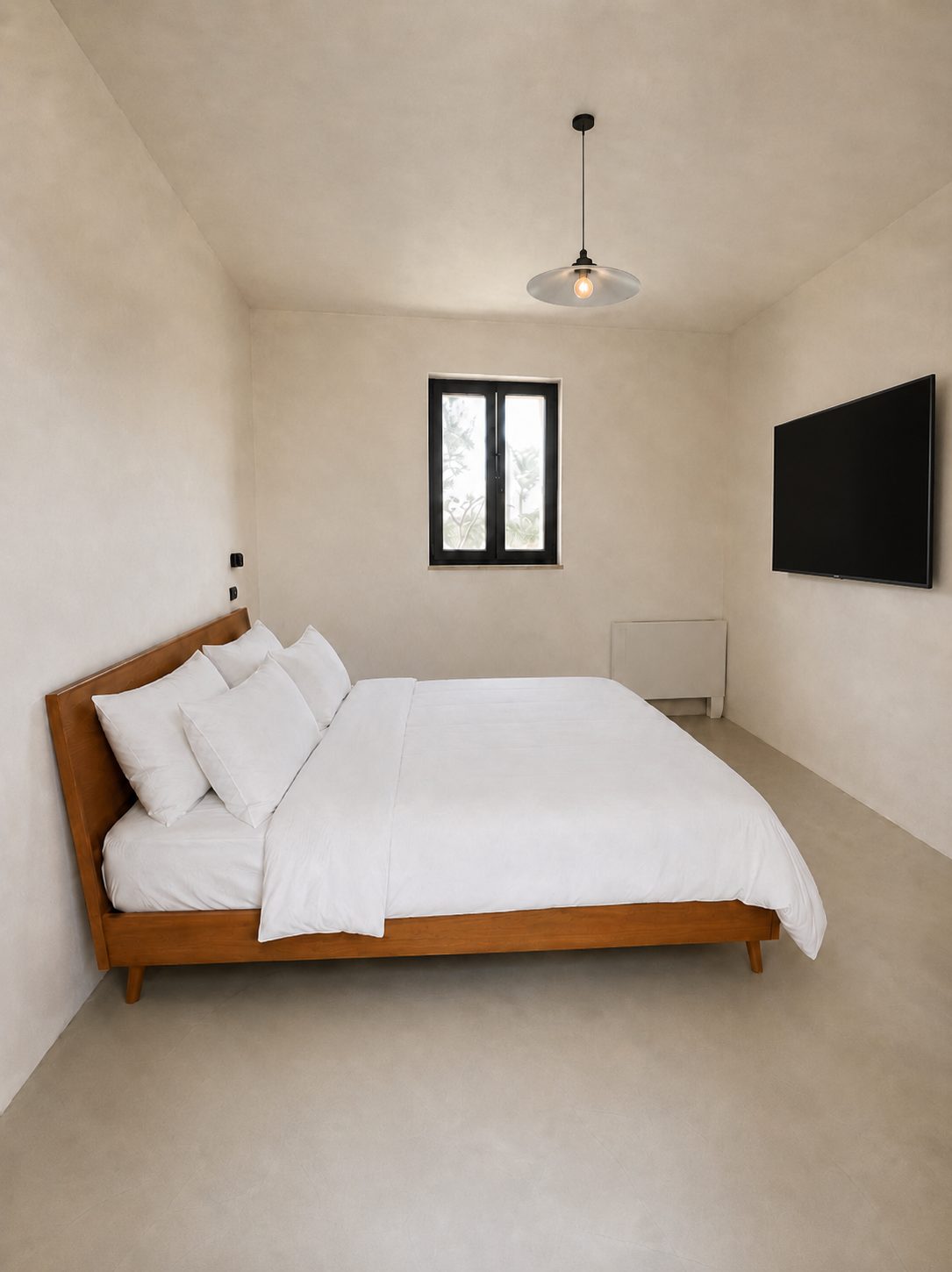 La deuxième chambre en suite de Casa Andrea — la même palette de microciment et le même lit en bois, une fenêtre à cadre noir, Pouilles.